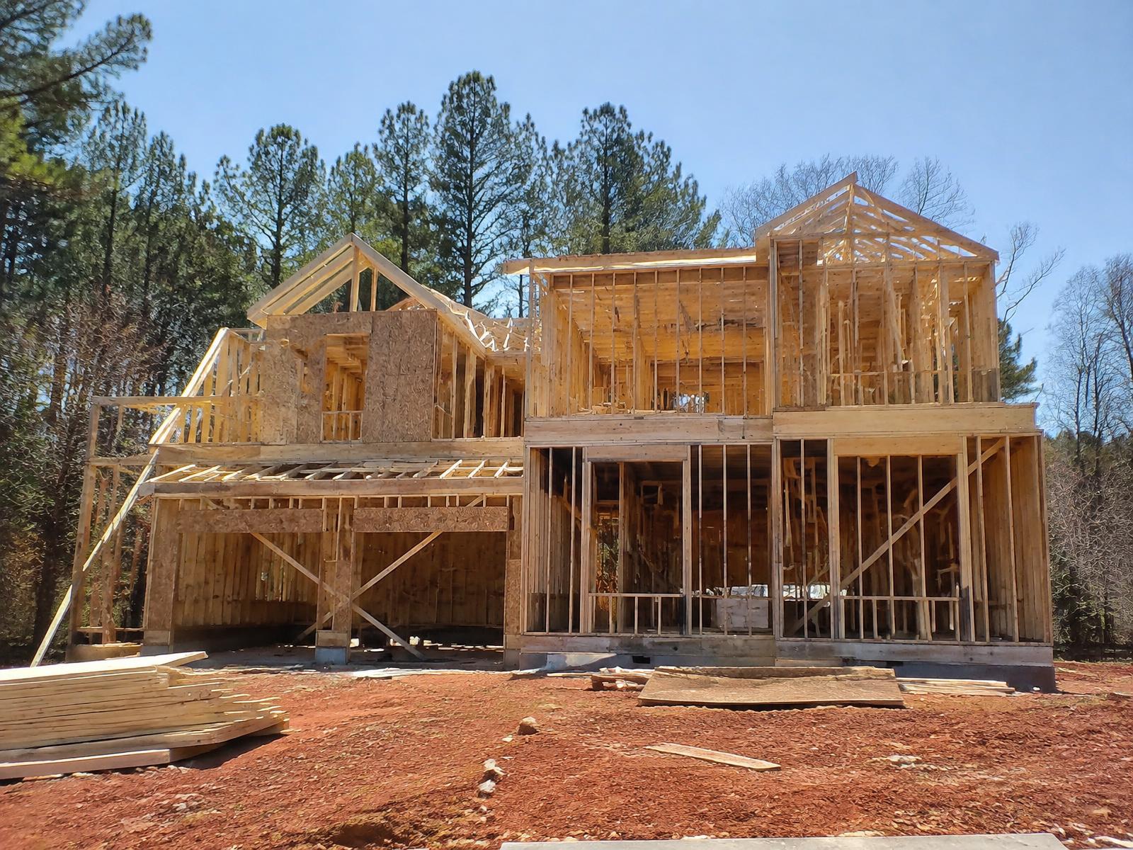 Two-story wood-framed home under construction on a red-clay lot (illustrative image)