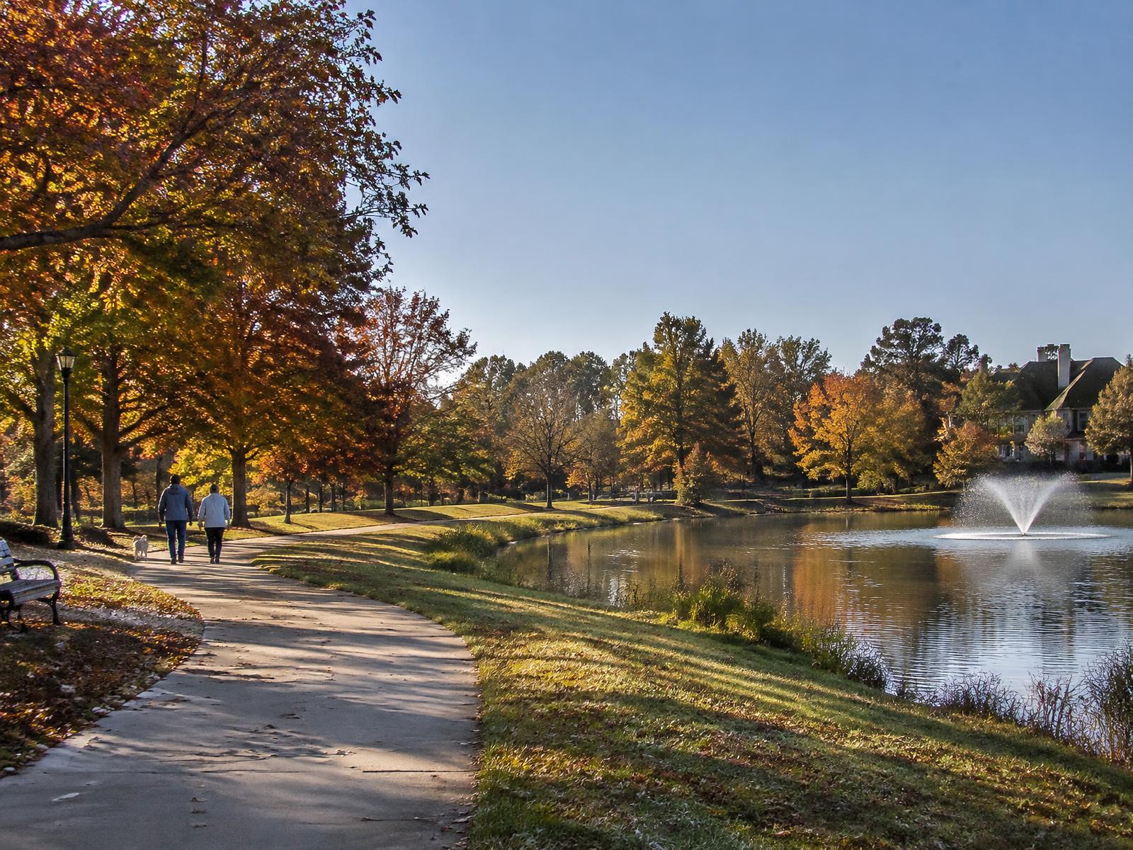 Lakeside walking path with autumn trees and a fountain (illustrative image, not a specific local park)